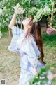 A woman in a blue kimono standing in front of a tree.