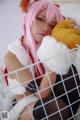 A woman with pink hair sitting in a cage with a teddy bear.