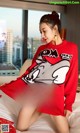 A woman in a red sweater is sitting on a bed.