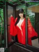 A woman in a red robe is looking out of a window.