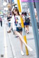 A woman leaning against a yellow pole on a city street.